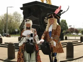 Zwei Personen, gekleidet in historische Trachten, auf Segways vor einer großen Statue